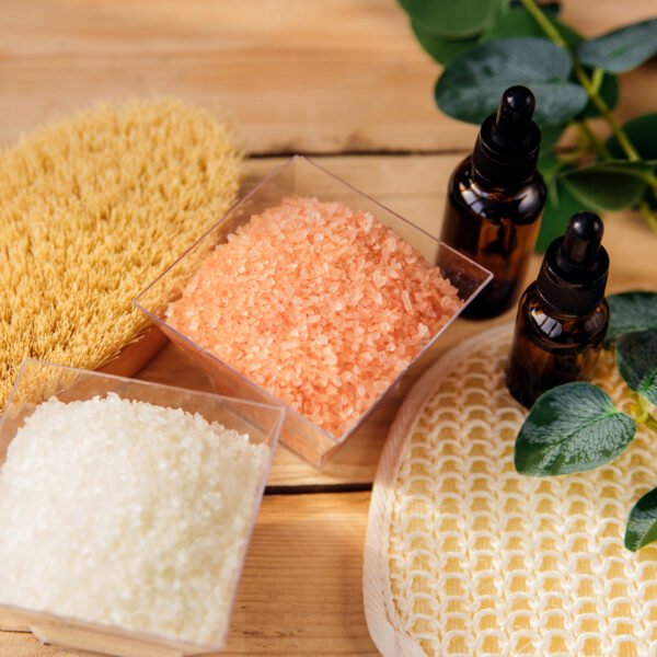 Eucalyptus, body scrubber, sea salt, and pink Himalayan sea salt on a wooden board
